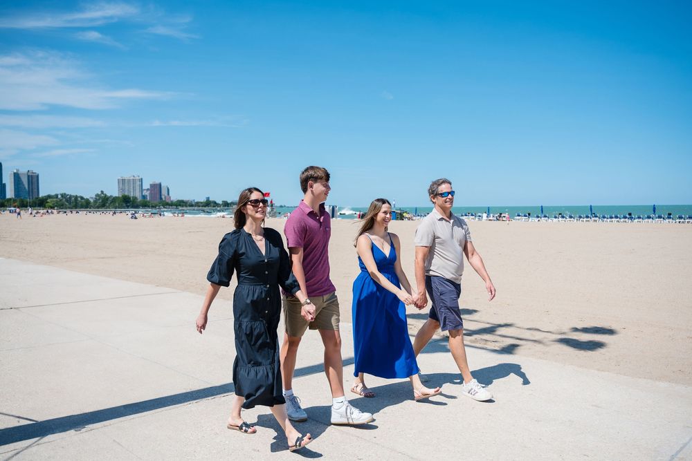 A family walking on a sunny beach with clear blue skies and white sand stretching into the distance.