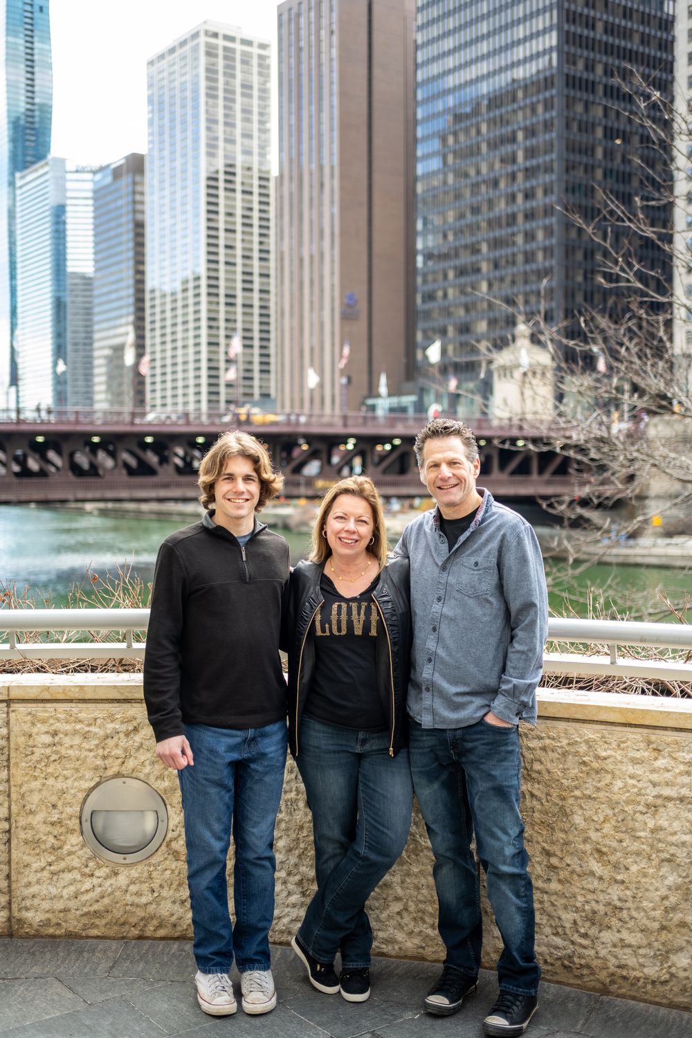A Family stands together along a stone wall with Chicago's iconic downtown skyline and river in the background.