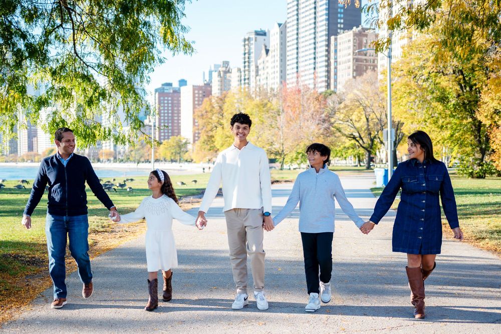 A family walk together on a path through an autumn park with city buildings visible in the background.