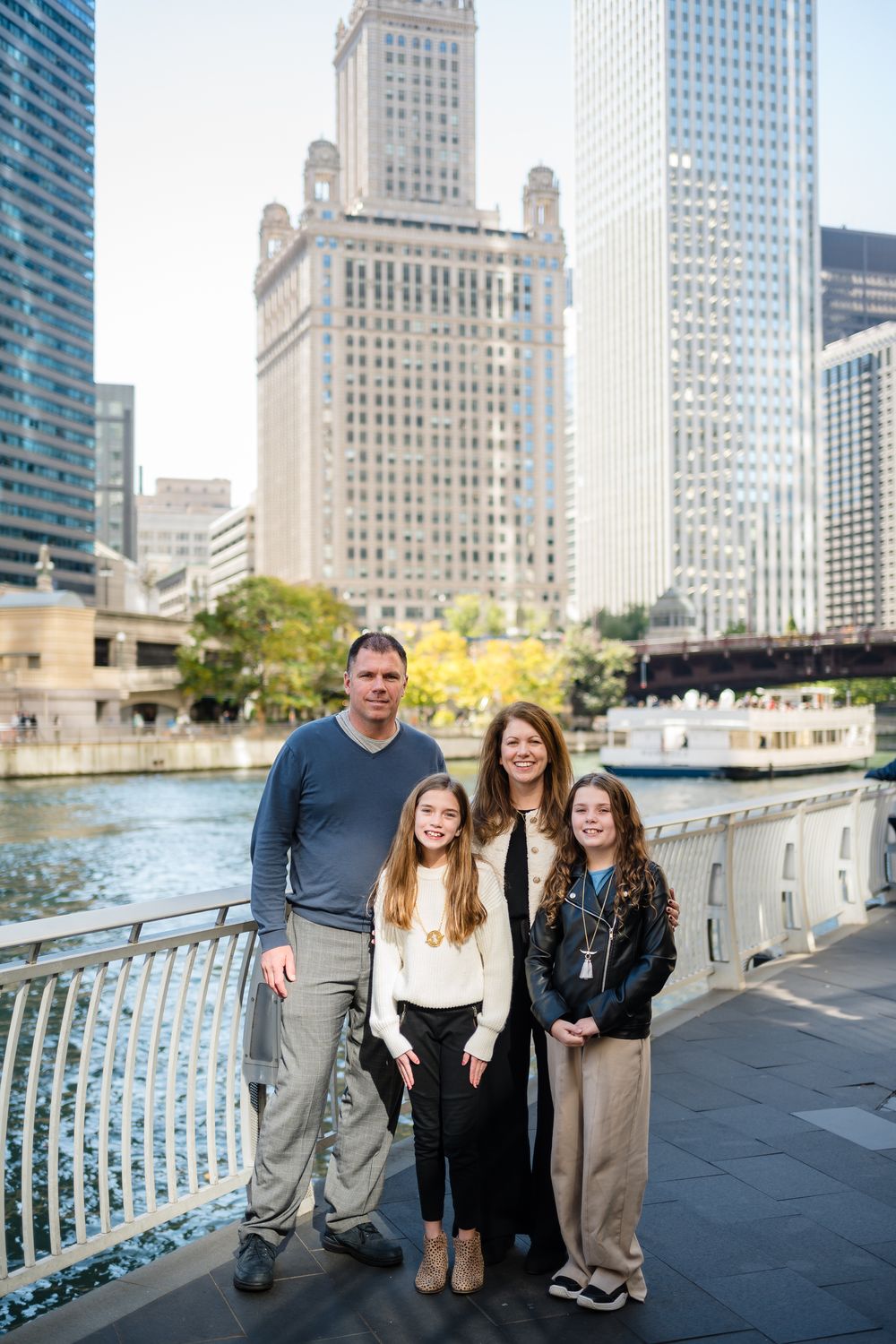 A family poses along the Chicago Riverwalk with downtown skyscrapers and buildings in the background.