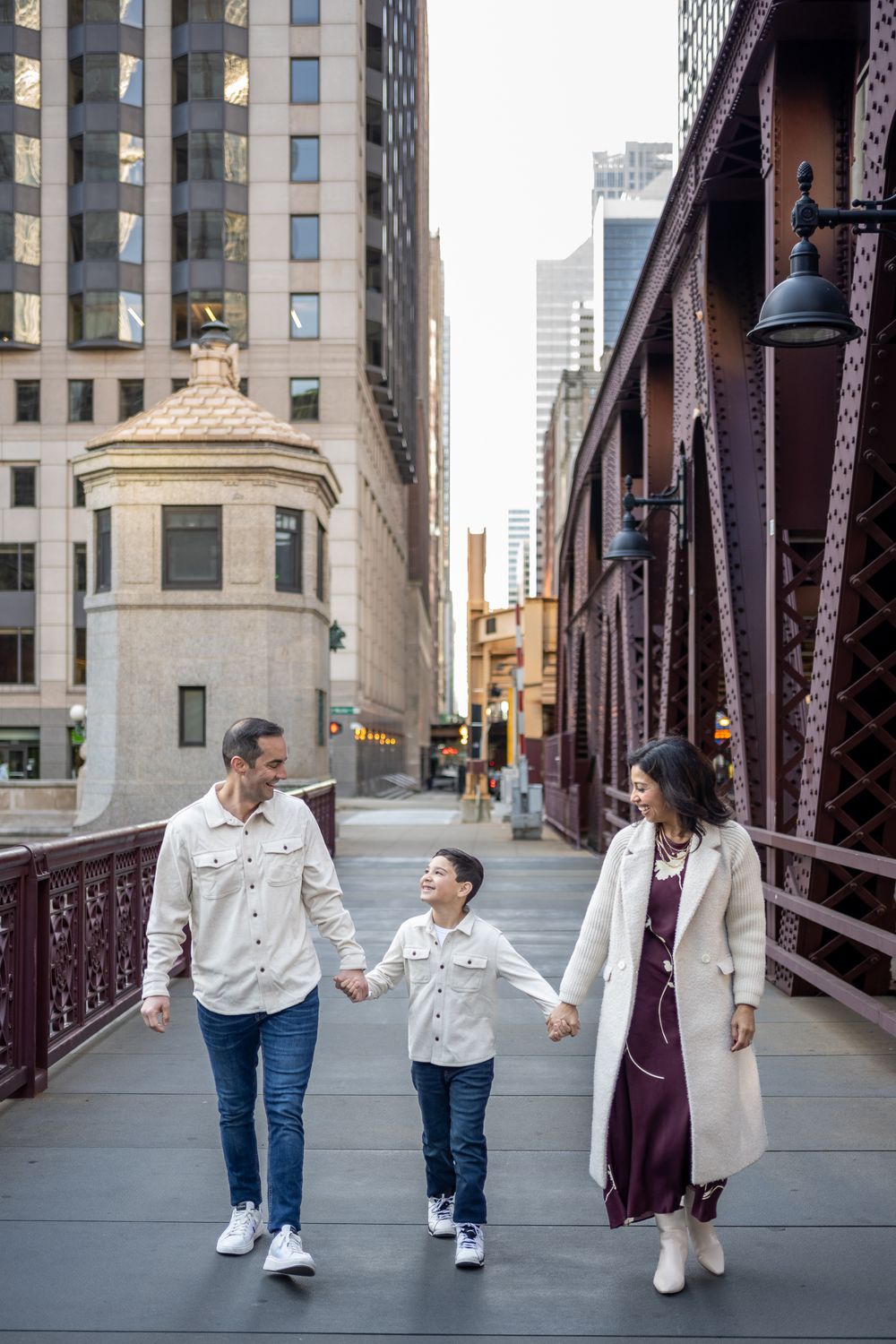 Family walking together holding hands on an urban bridge in downtown Chicago with tall buildings in background.