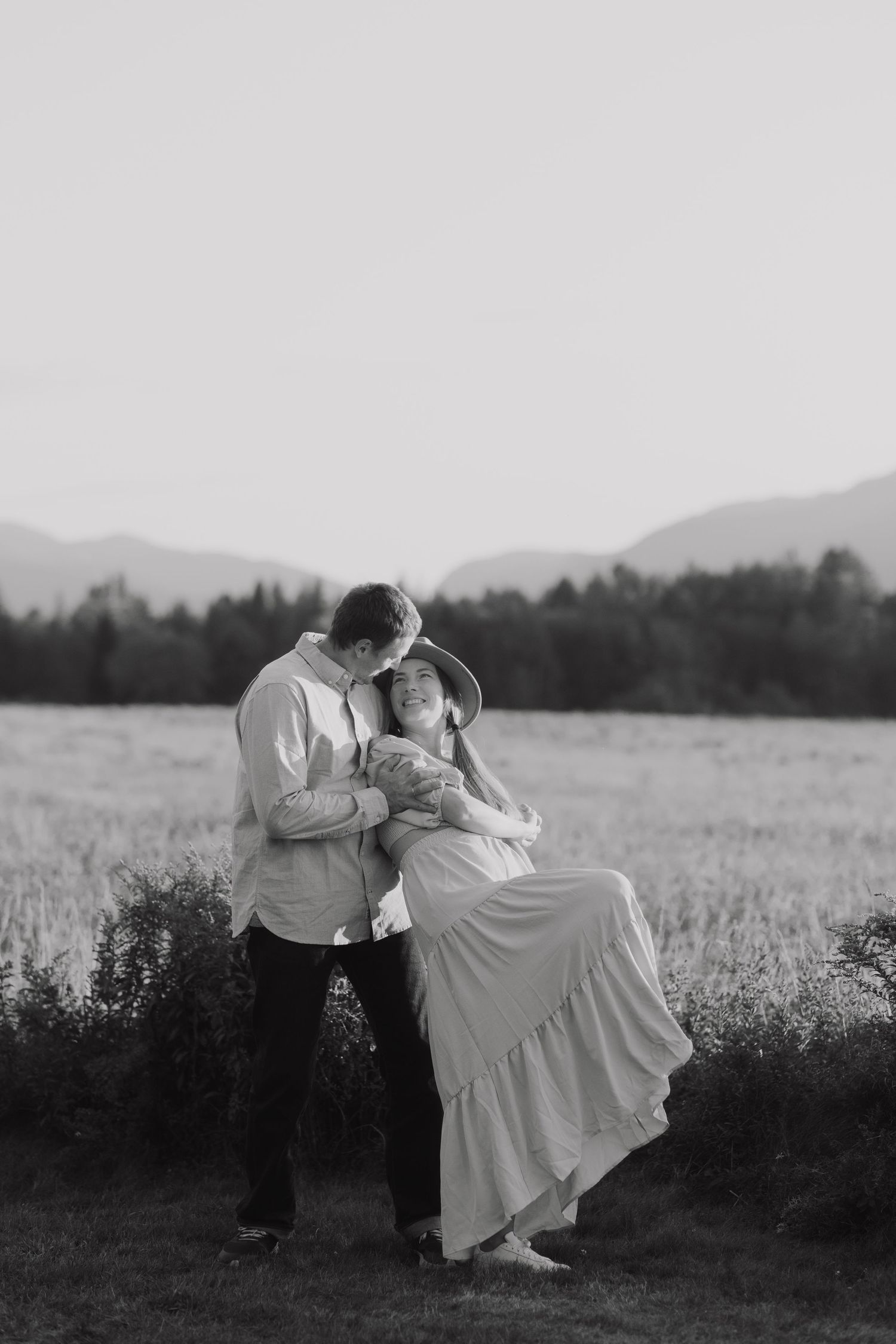 A couple dances together in a romantic black and white scene across a meadow with mountains in the background.