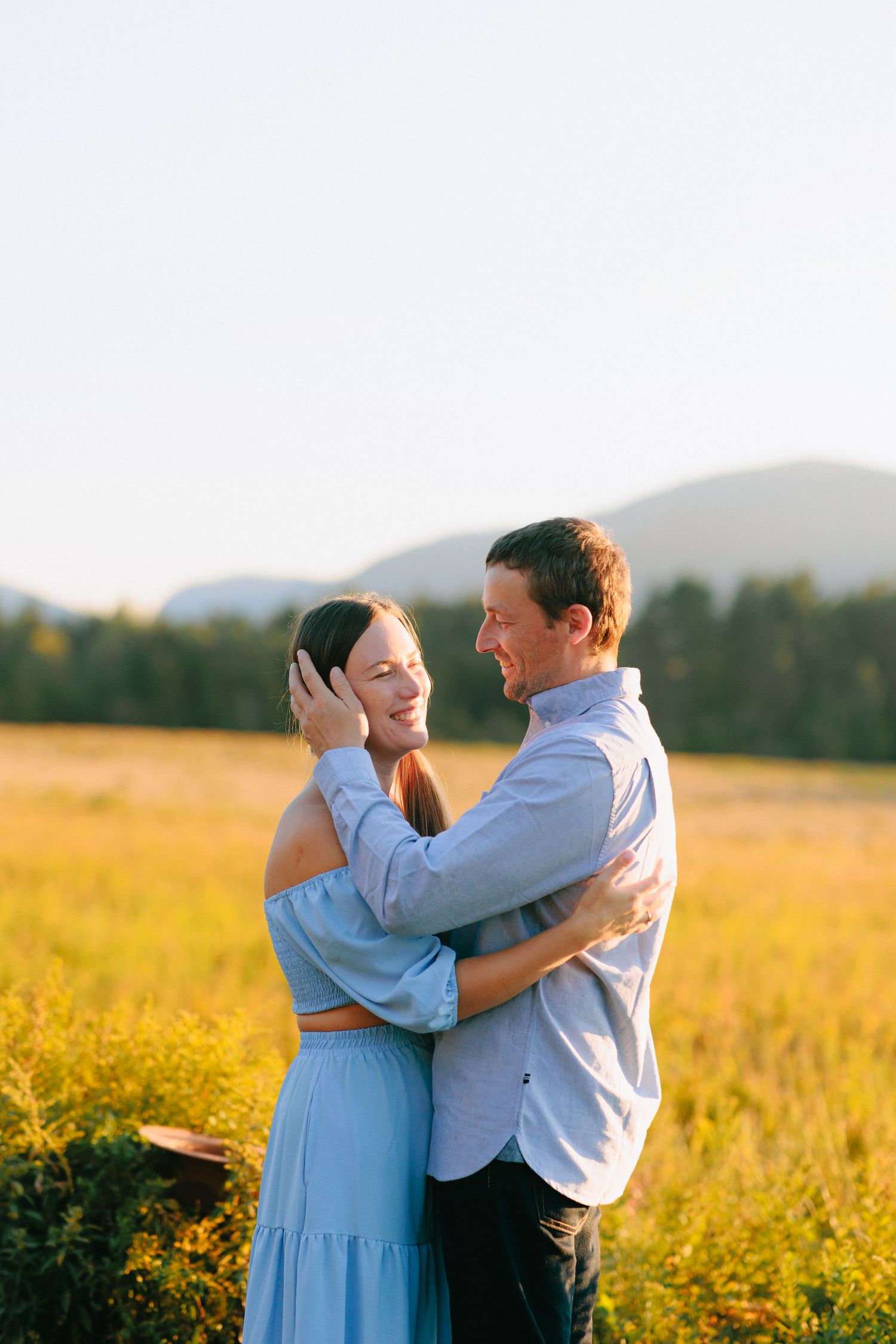 A couple dancing and embracing in a golden field at sunset with mountains in the background.