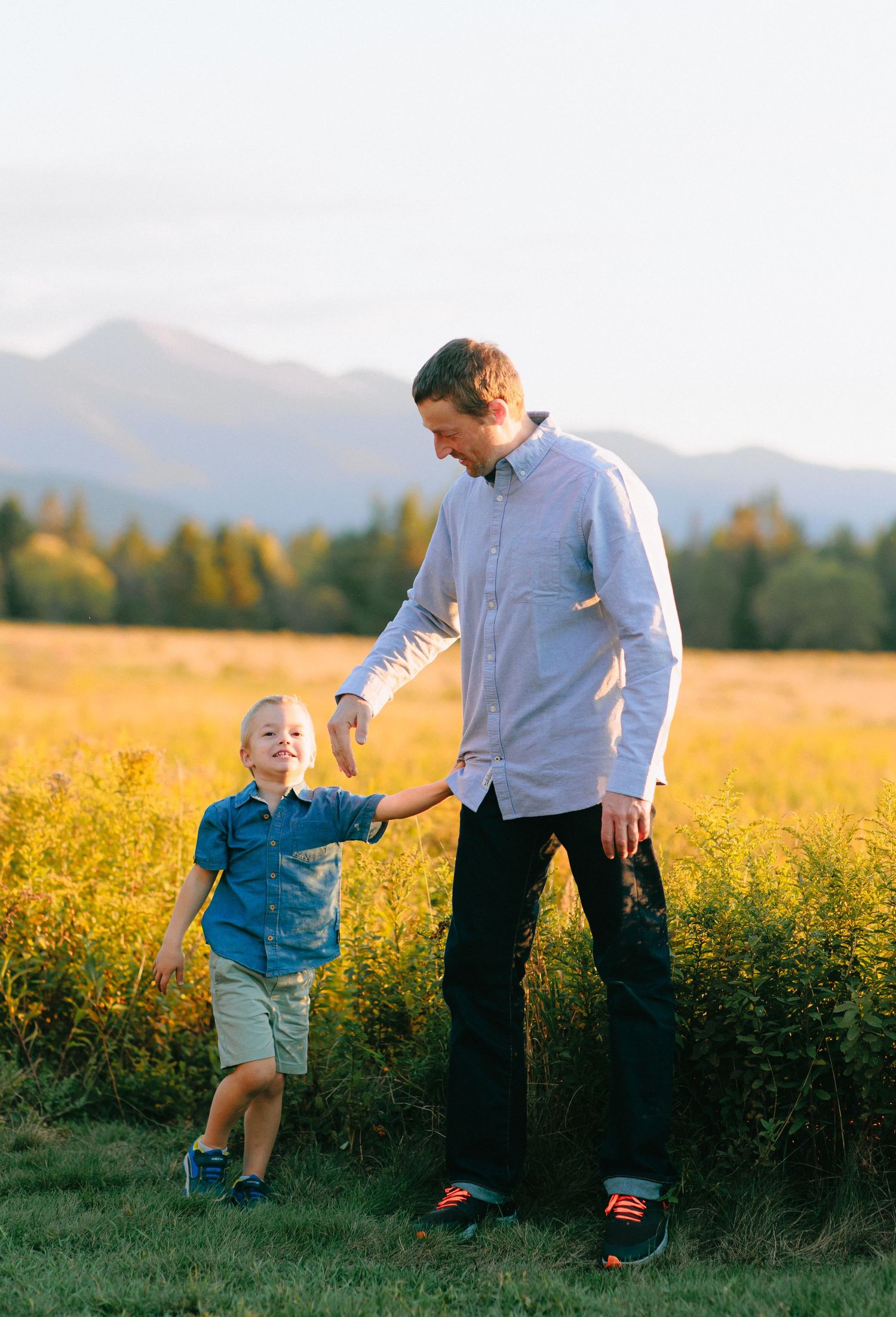 Family playing and running together in a golden field with mountains in the background.