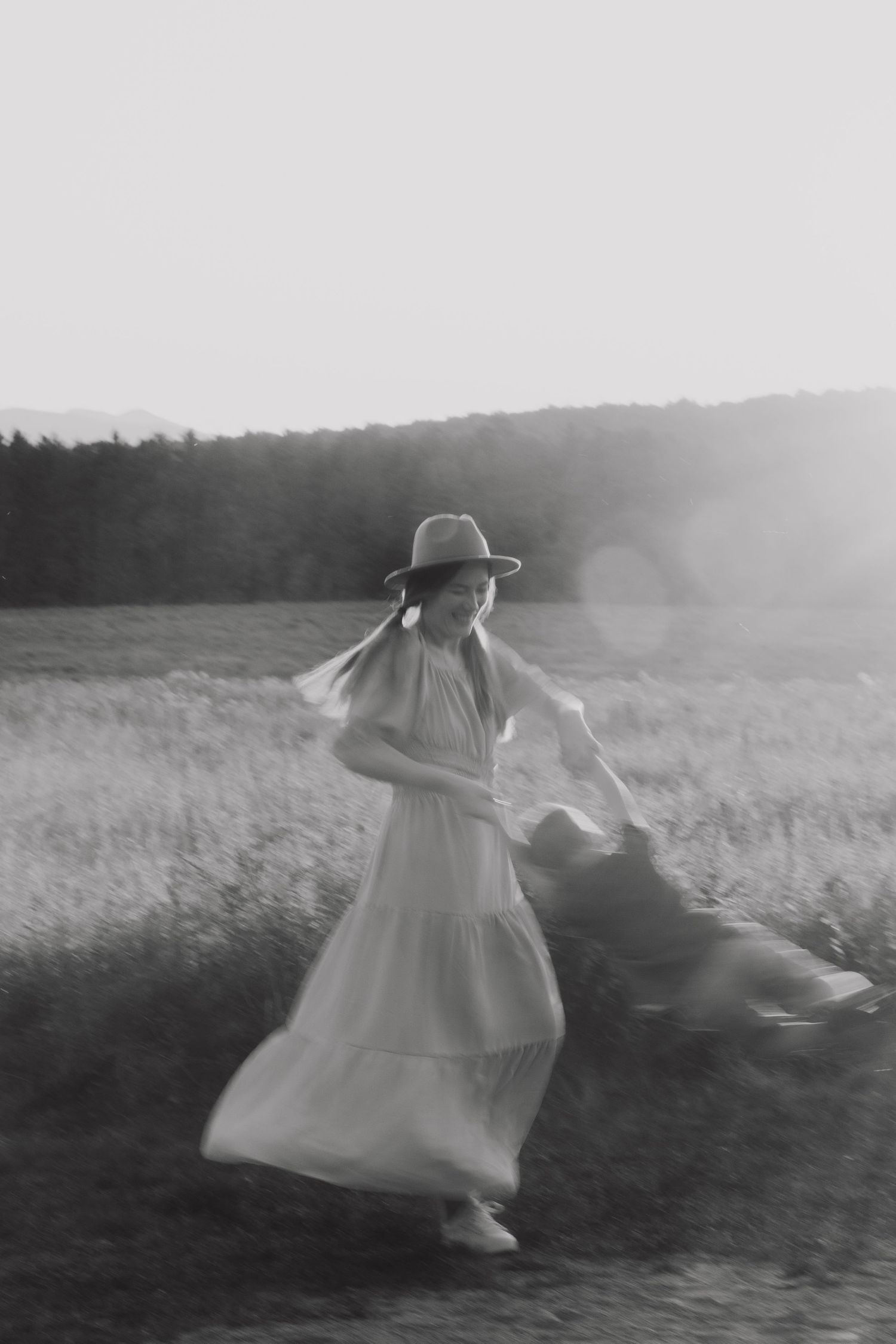 Ethereal figures in flowing white dresses dance through a dreamy monochrome field at dusk.
