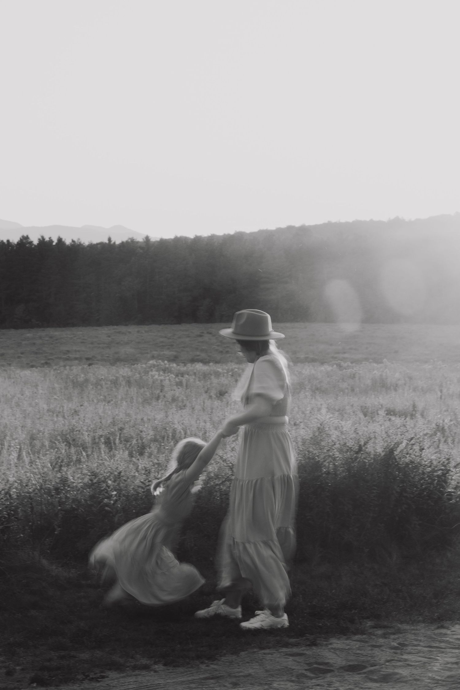 Two people in light clothing relax in a peaceful meadow during a misty black and white afternoon.