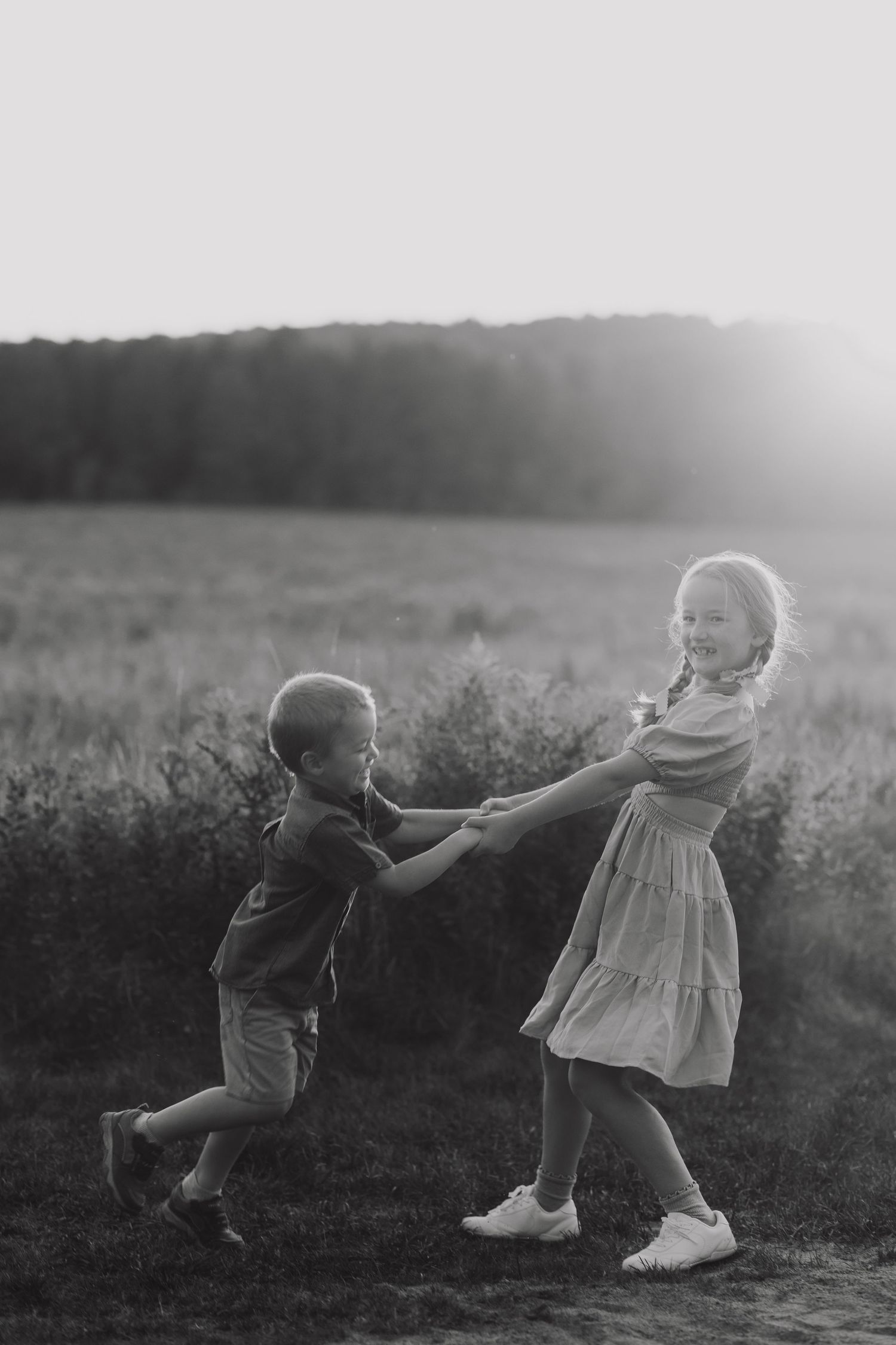 Two children play and spin together in a sunlit field during golden hour.