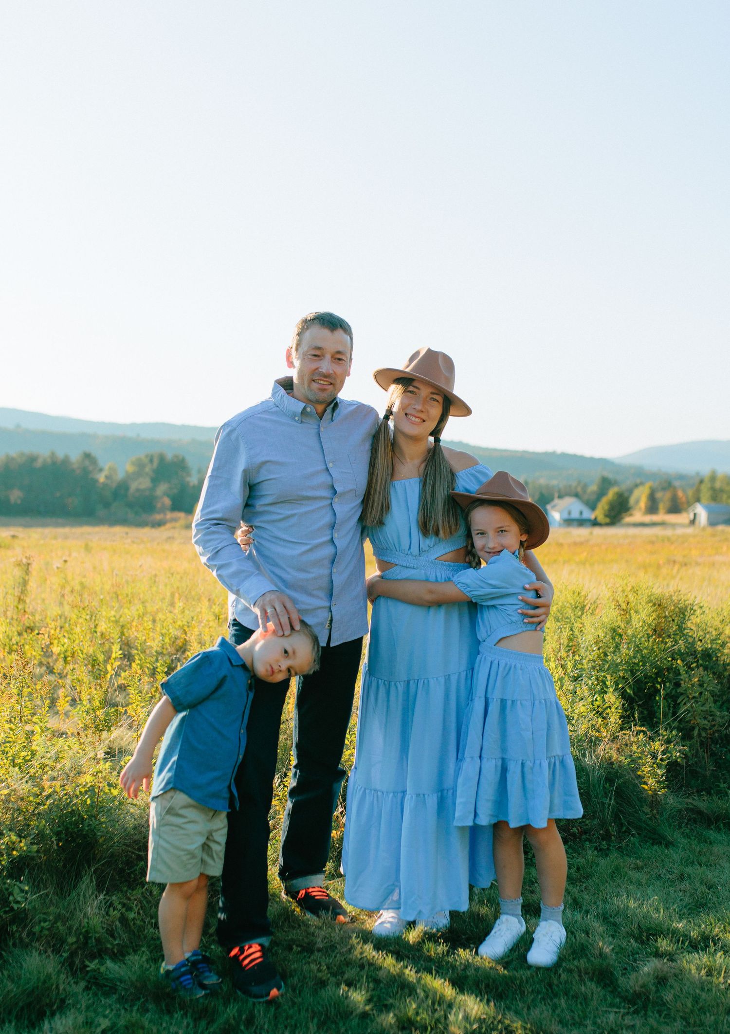 A group in coordinated blue outfits poses together in a sunny meadow during golden hour.