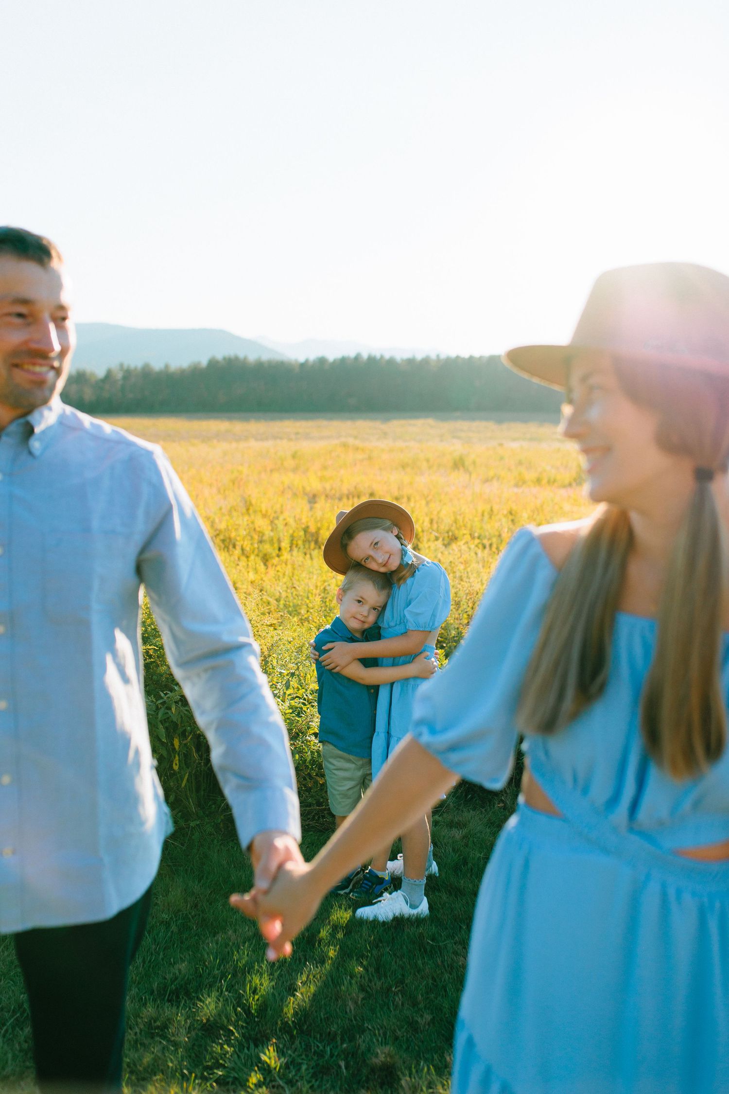 Family enjoying playful moments together in a sunlit yellow field wearing coordinating blue outfits.