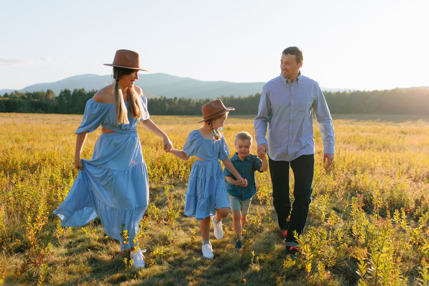 A family holds hands while walking through a sunlit meadow at golden hour.