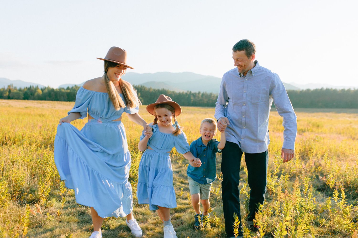 Family members in coordinating blue outfits walk together through a wildflower field at sunset.