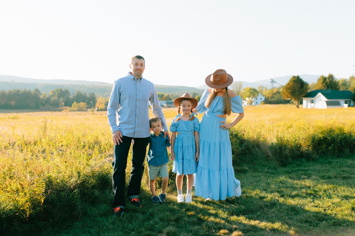 Family wearing coordinated blue and white outfits walks together through a golden sunlit field at sunset.