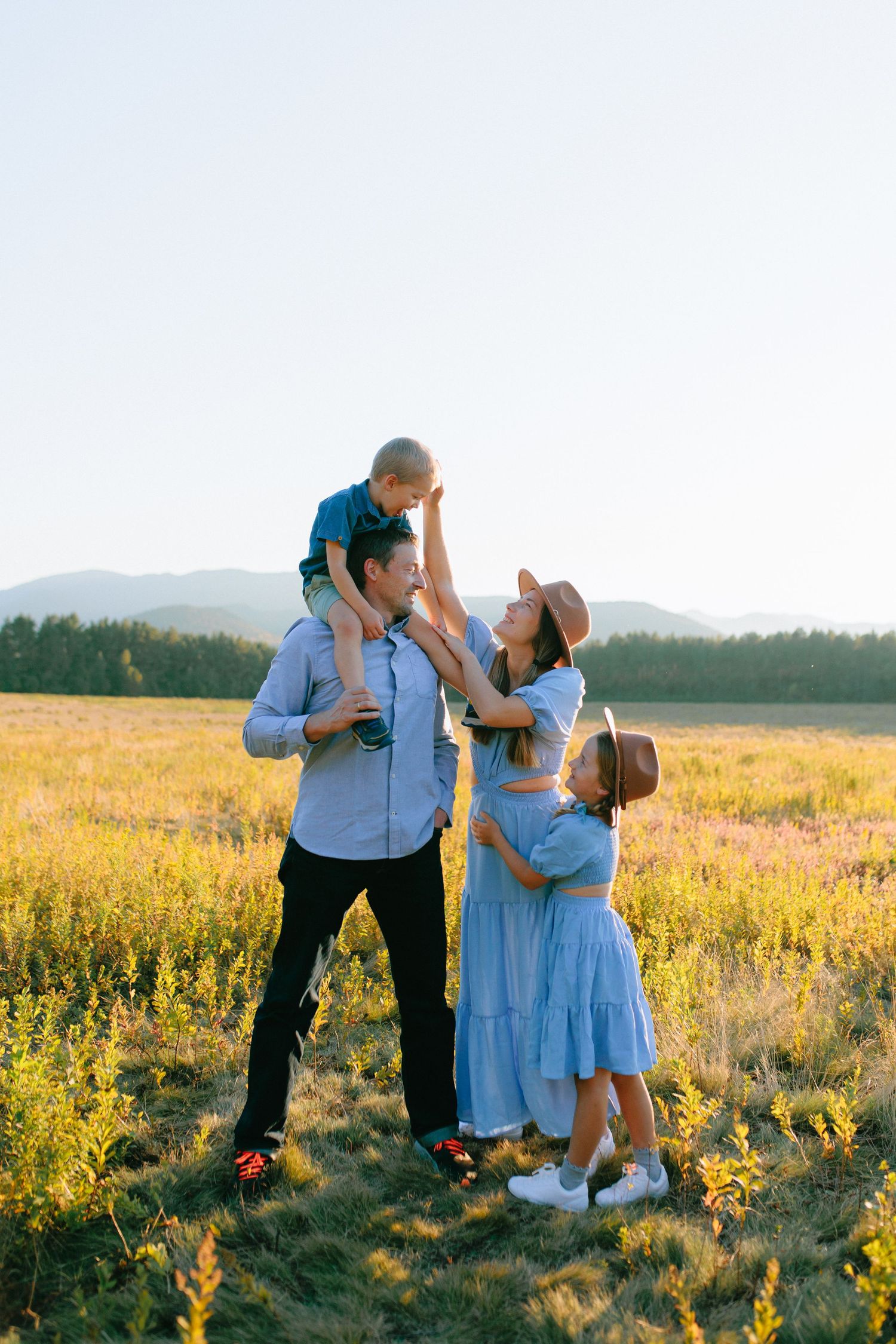 A couple shares tender moments in a golden field at sunset with mountains in the background.