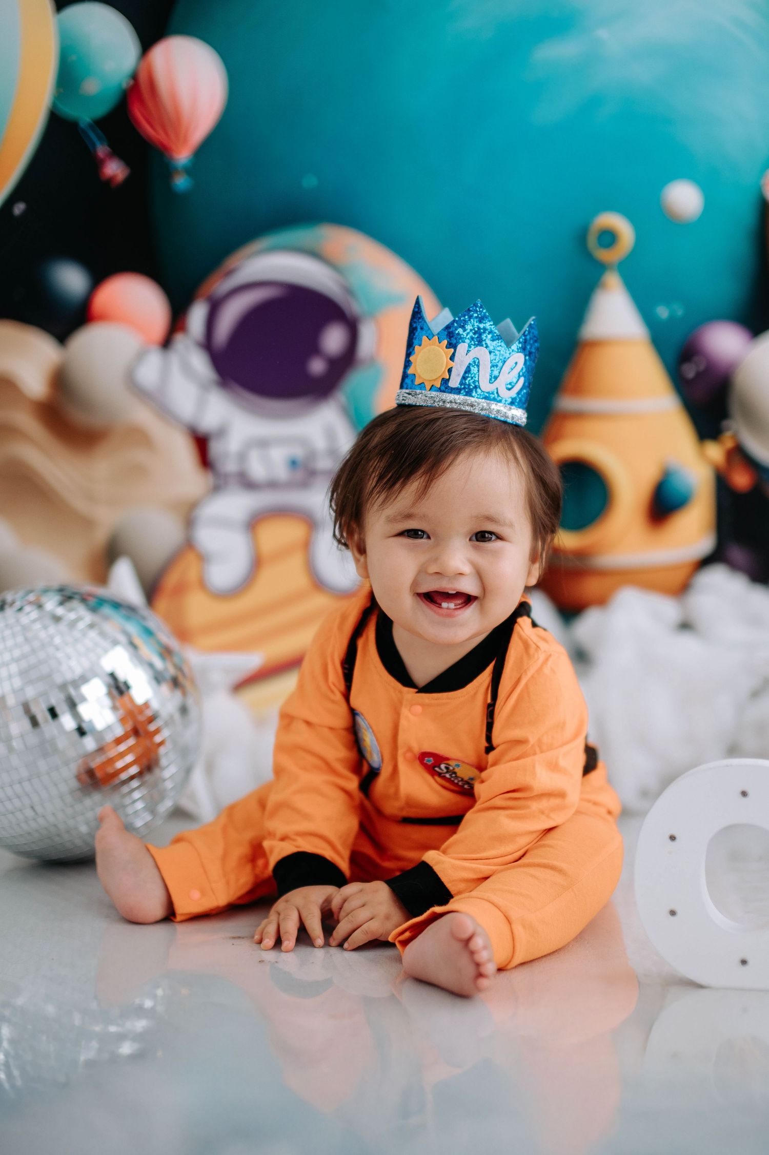 Charming astronaut-themed portrait with decorative planets, stars, and teal backdrop creating magical space scene.