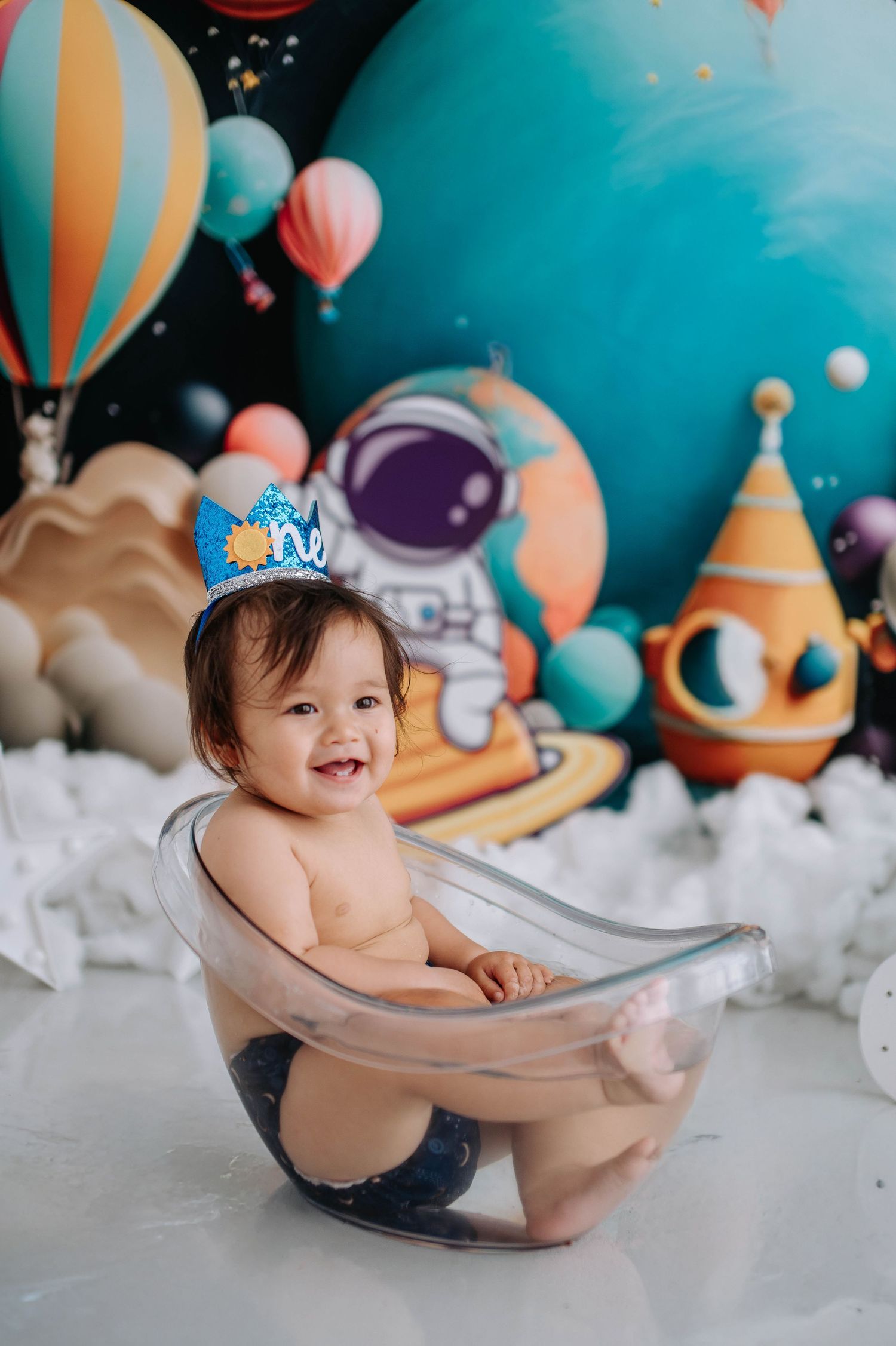 Colorful space-themed birthday setup with balloons and decorations featuring an astronaut backdrop and clear seating prop.