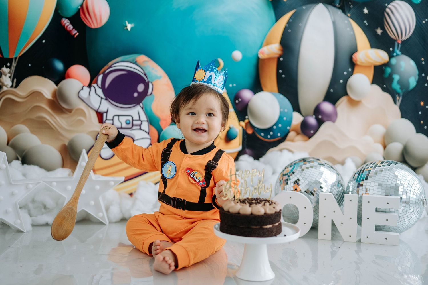 Adorable baby cake smash photo session with orange and teal decorations featuring balloons and plush toys.