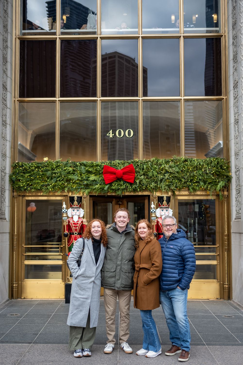 Family standing in front of a modern office building entrance with glass doors and holiday greenery decorations.