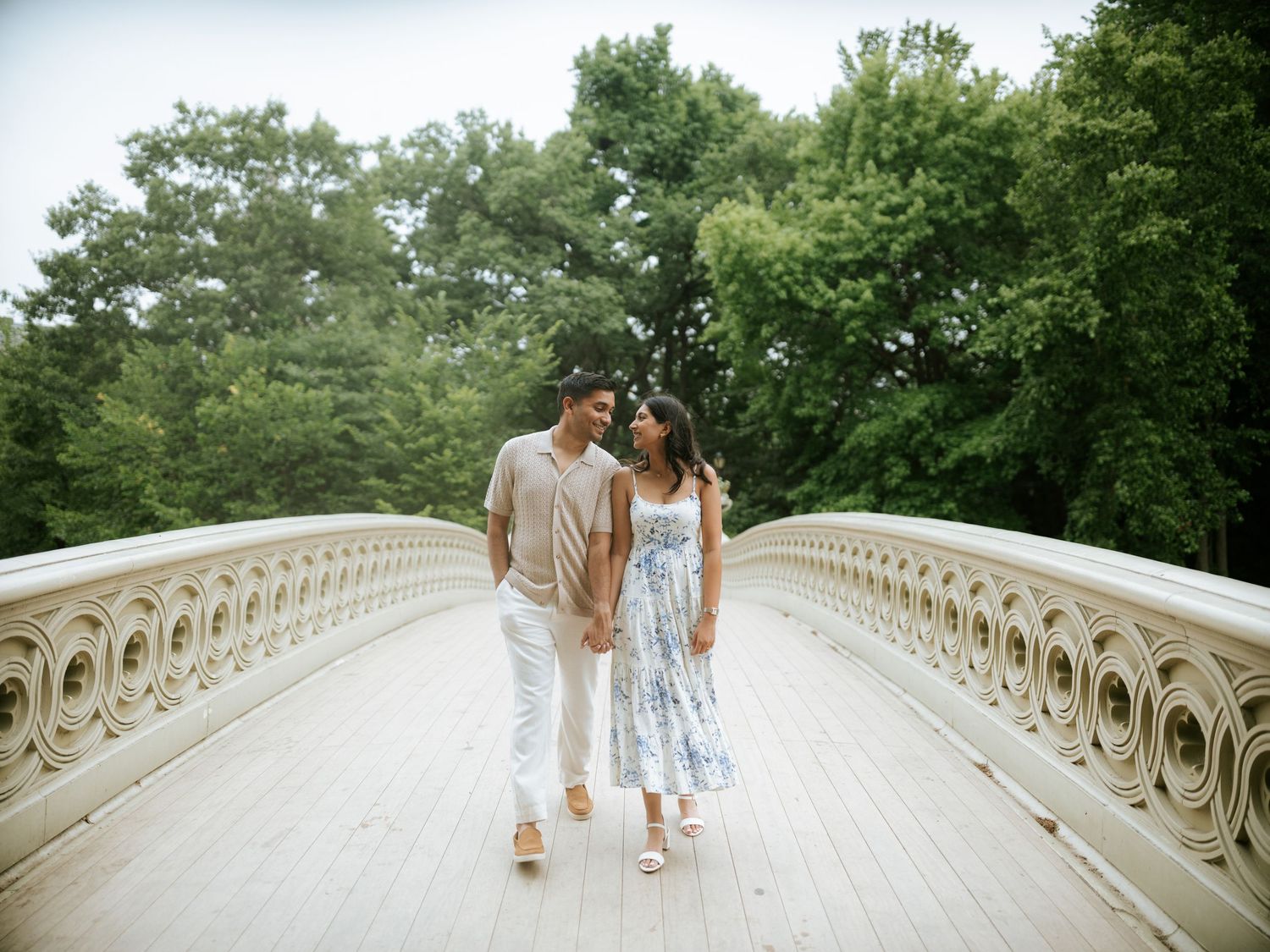 A couple walks together on the ornate Bow Bridge in Central Park during a summer afternoon.