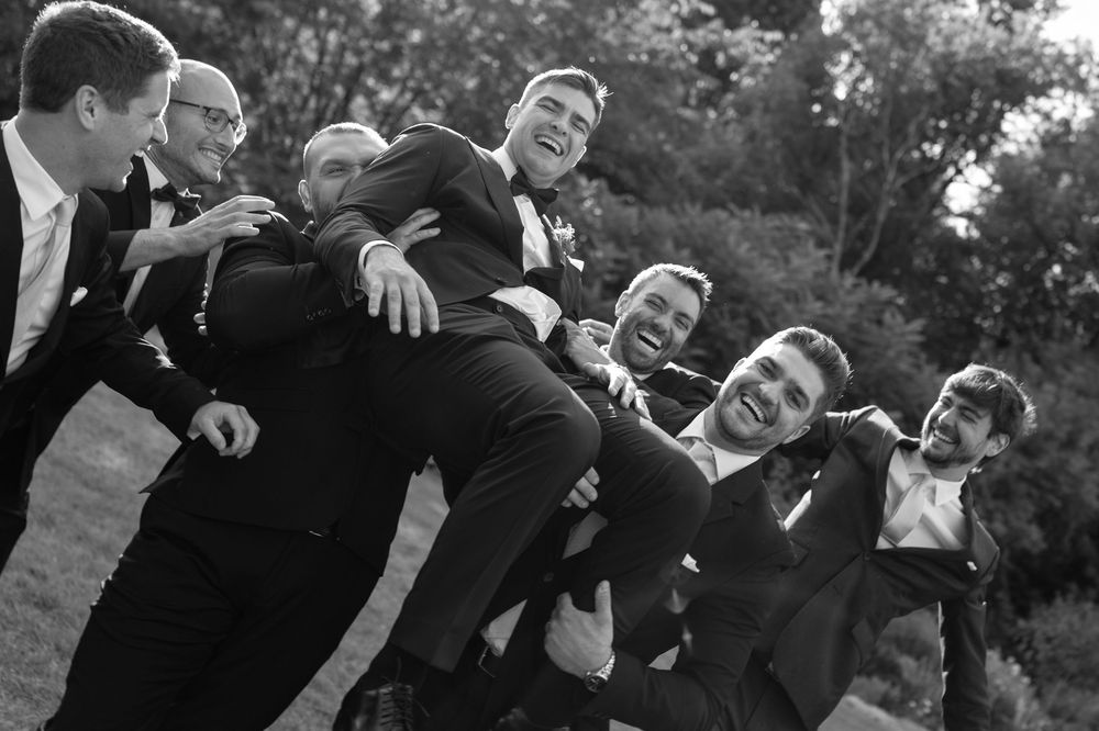 A sequence of black and white photos showing groomsmen laughing and having fun during a wedding photoshoot outdoors.