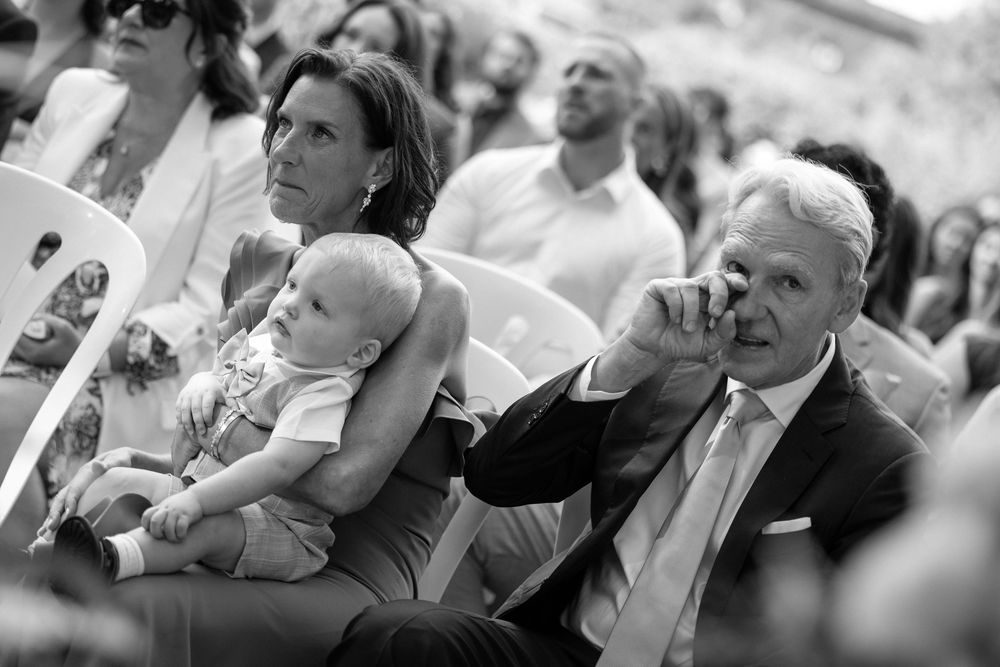 A black and white photo shows a row of people seated at what appears to be a formal event or gathering.