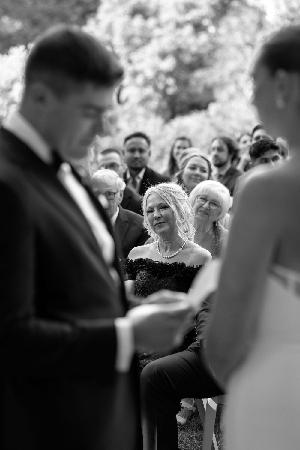 Black and white candid photo showing guests mingling and laughing during an outdoor wedding reception.