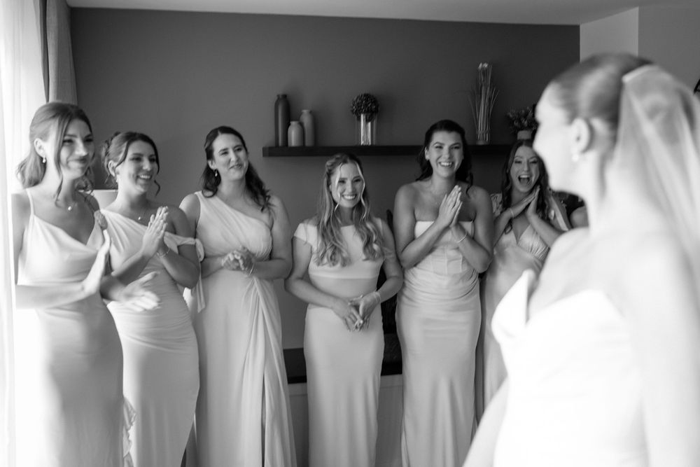 A row of bridesmaids in white dresses stand together getting ready for a wedding celebration.