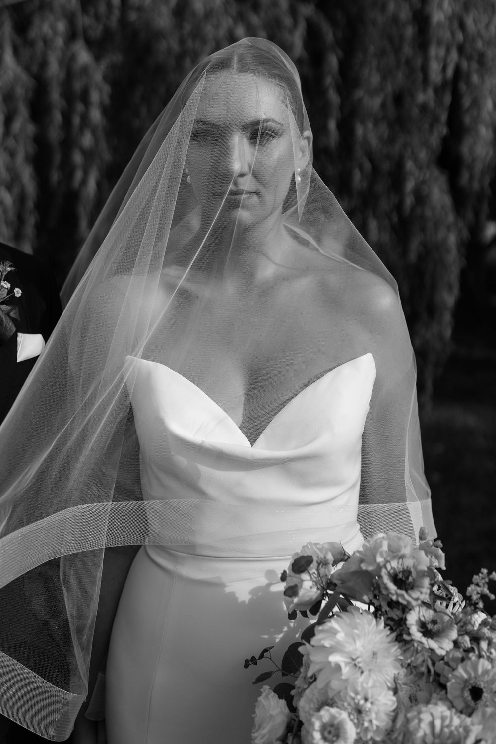 Bride in classic white sweetheart neckline gown with flowing veil holds elegant bouquet of white and purple flowers.