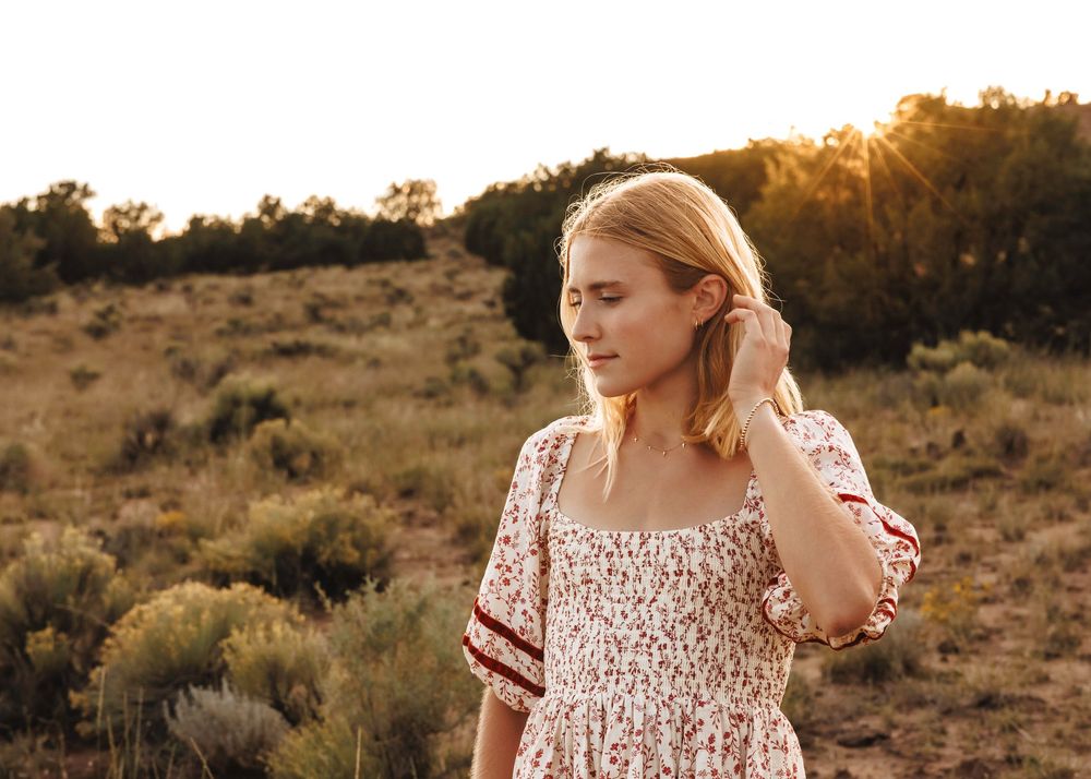 Blonde woman in floral dress touching hair at golden sunset in desert field.