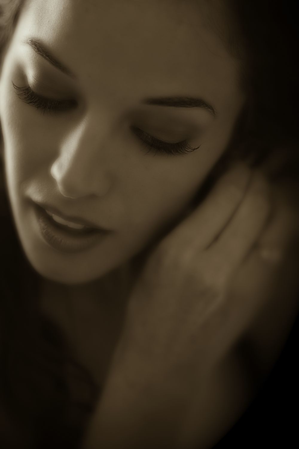 Artistic sepia portrait showing a person with closed eyes and gentle expression in contemplative pose.