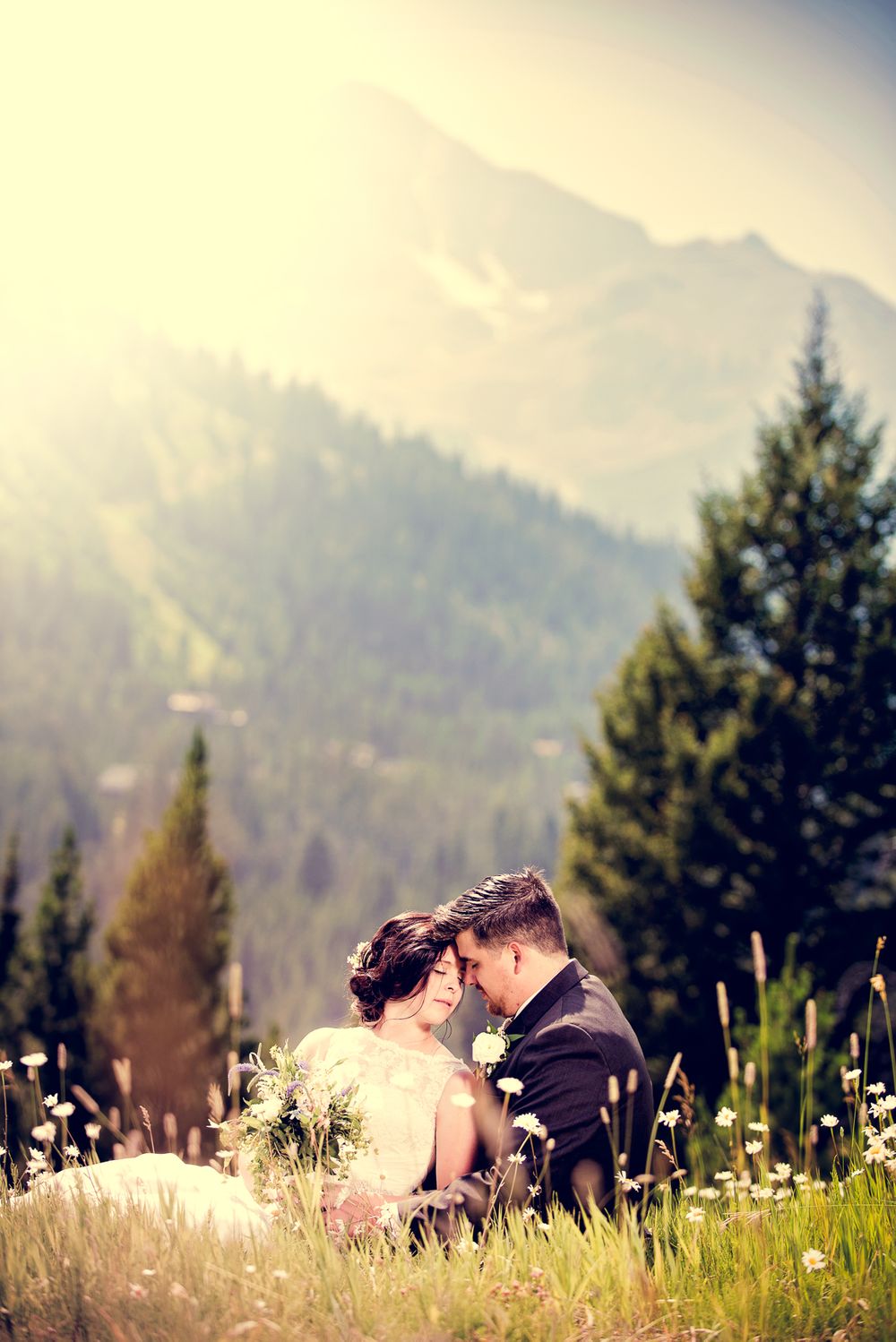 A romantic mountain wedding photo with evergreen trees and misty peaks in the background.