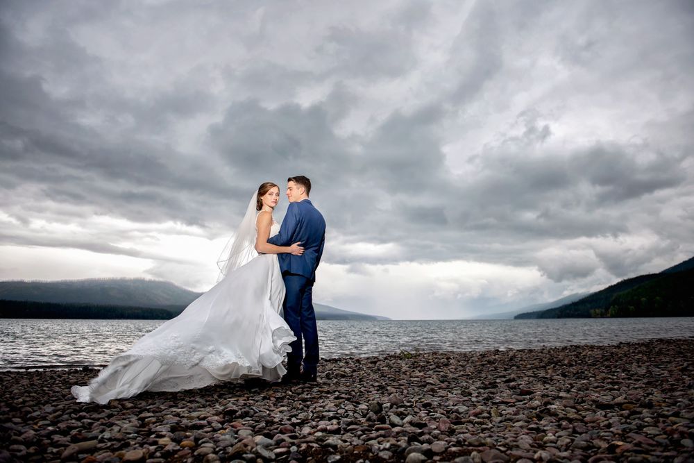 Dramatic wedding portrait by a lake with stormy clouds and mountains in background.