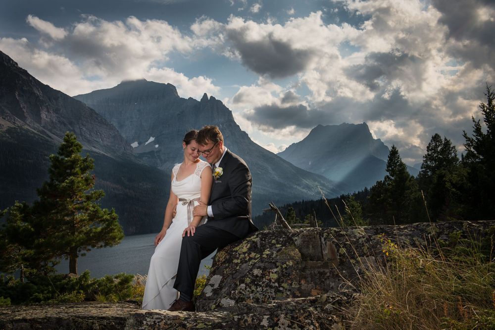 Wedding couple embracing on rocky outcrop with dramatic mountain peaks in background.