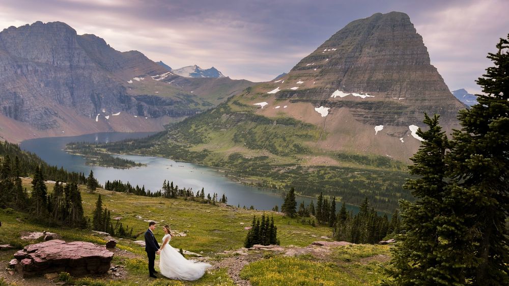 Panoramic mountain landscape with dramatic purple sunset sky over rocky peaks and alpine meadows at Glacier National Park.