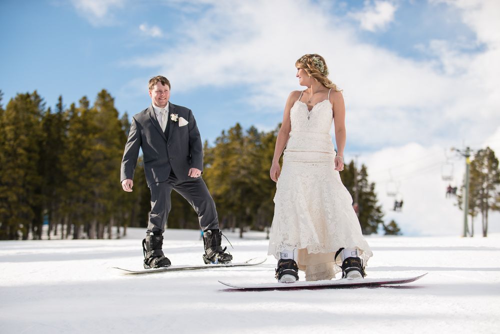 Adventurous couple snowboarding together in formal wedding attire on a winter mountain slope.