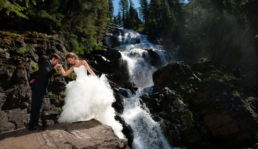 Wedding photo at dramatic waterfall with cascading white water in forest setting.