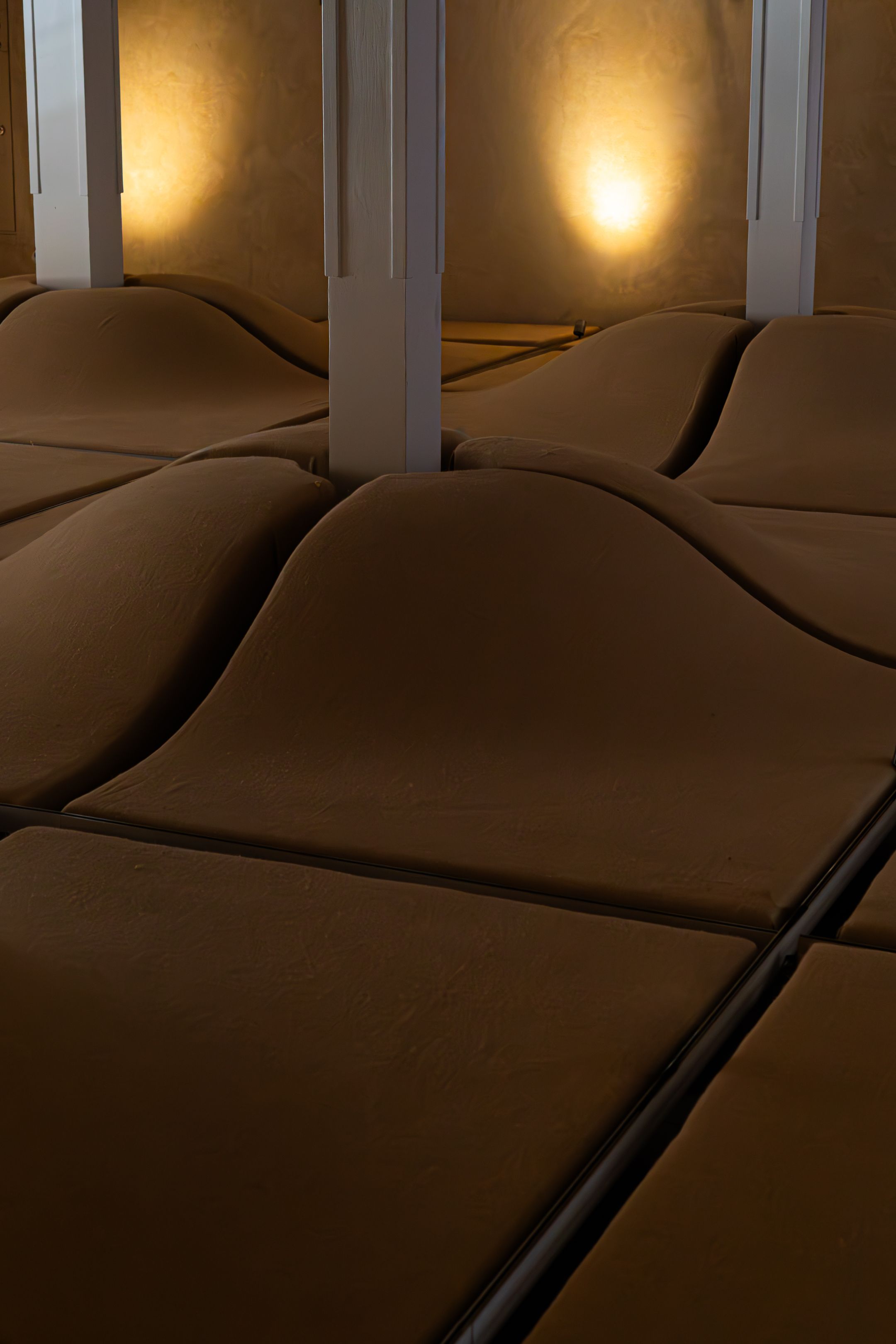 Dimly lit spa room with massage beds arranged in rows under warm ambient lighting.