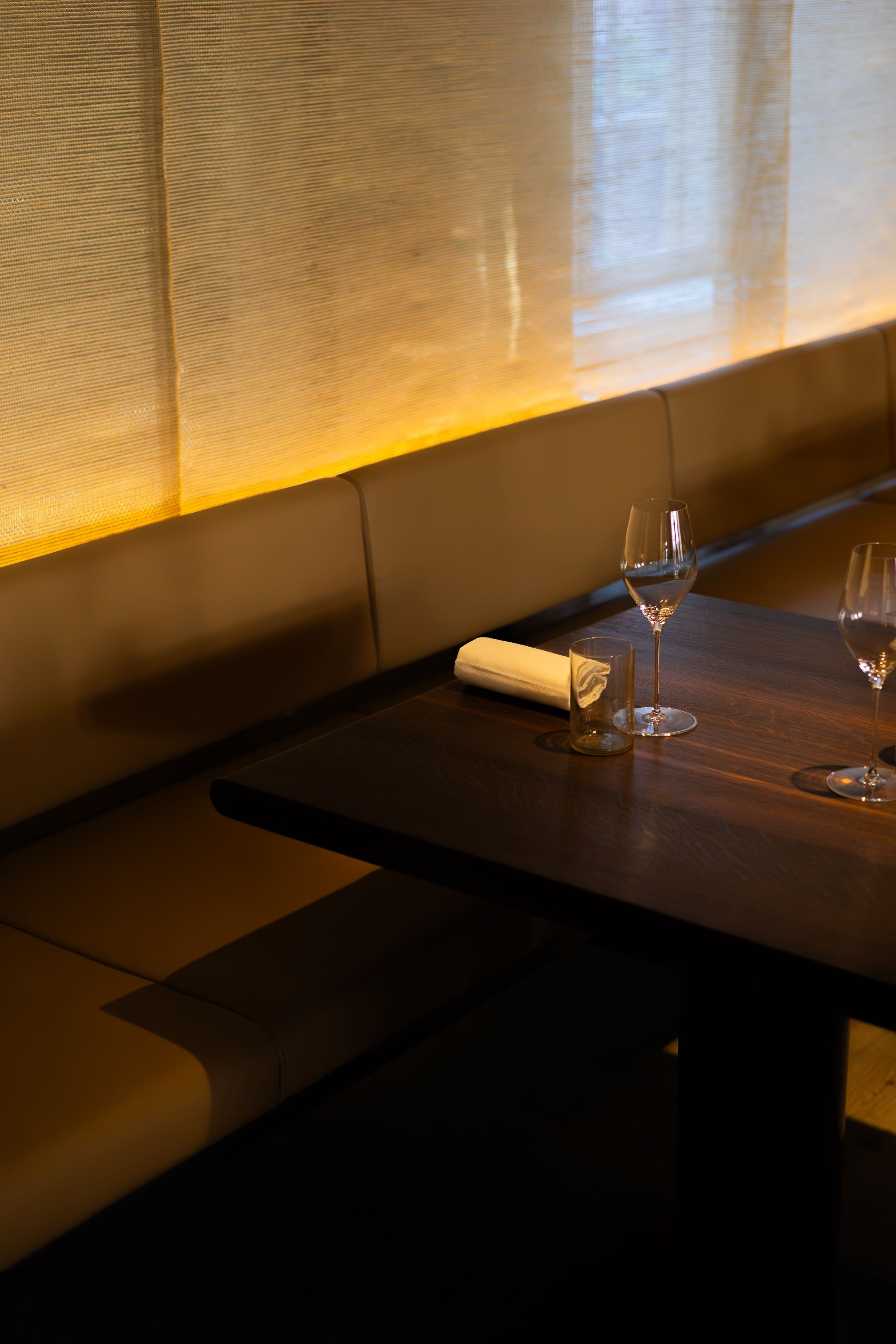 Modern restaurant interior with leather banquette seating and wine glasses on dark wooden tables.