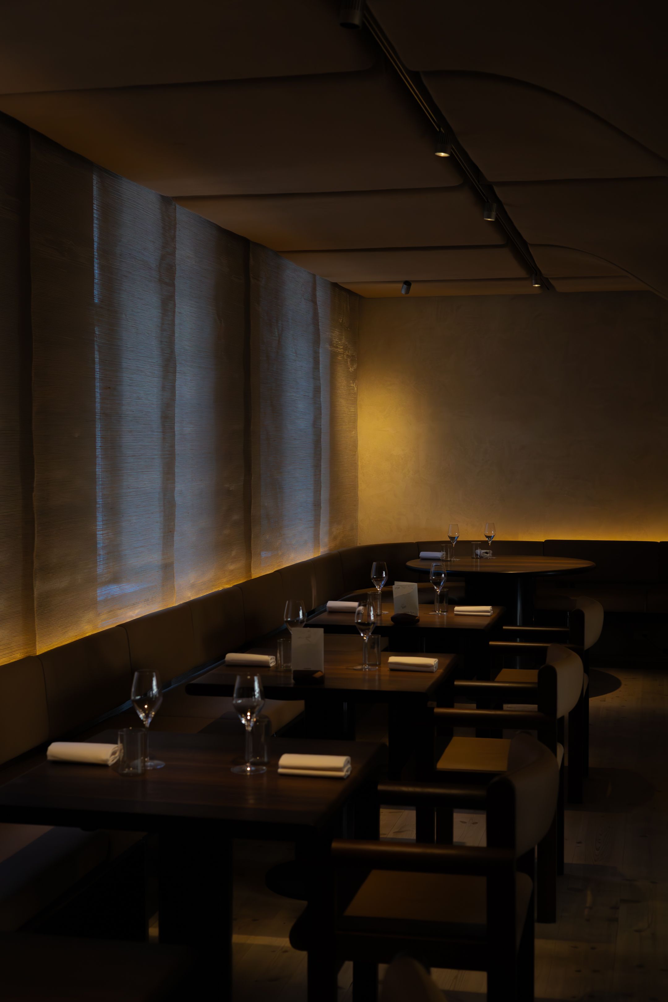 Dimly lit upscale restaurant interior with wooden tables and ambient wall lighting.