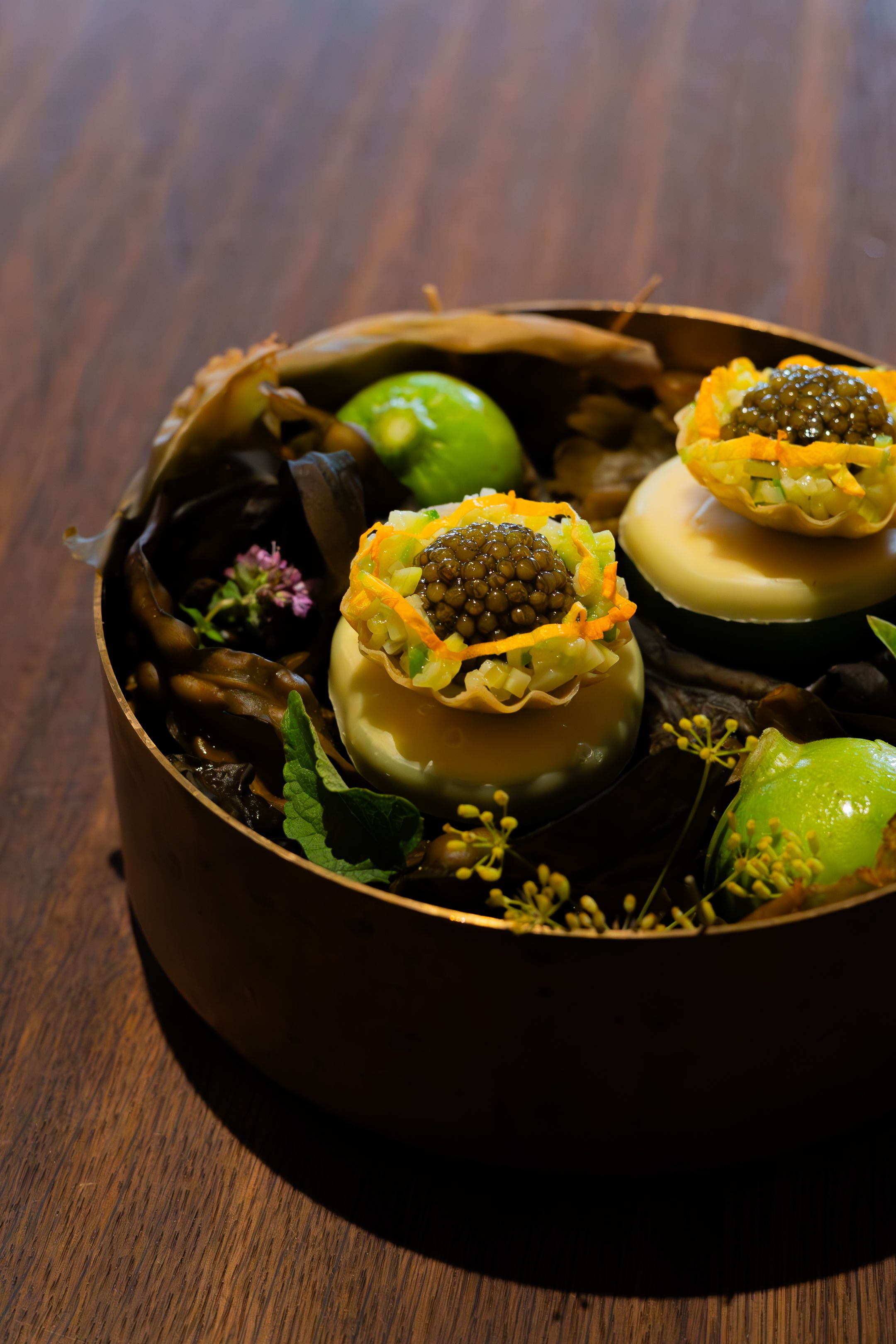 Artistic food plating of appetizers with yellow and green garnishes on a dark wooden surface.