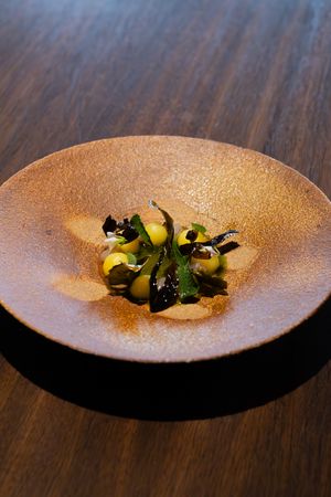 An artistic plating of small yellow and green garnishes on a textured ceramic plate against a dark wooden surface.