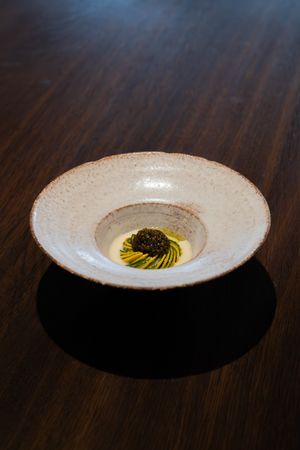 Textured white ceramic bowl with yellow oil and dark garnish on wooden table.