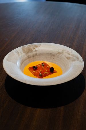 Orange soup with garnish served in a white ceramic bowl on dark wooden surface.