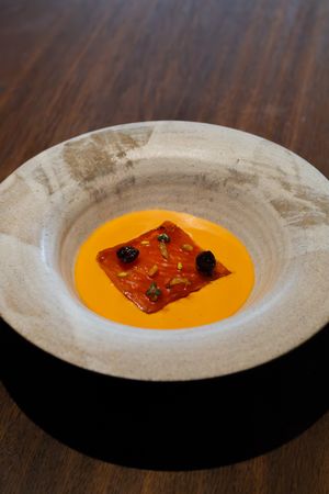 Vibrant orange soup with square garnish and dark accents in white ceramic bowl.