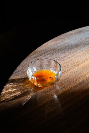 A glass cup of amber-colored whiskey or cognac sitting on a wooden surface in dramatic lighting.