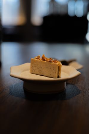 Close-up shot of a dessert slice on a white plate against a dark wooden table with soft bokeh background.