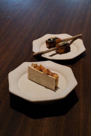 Elegant plated desserts featuring a slice of cheesecake and chocolate-covered bites on white plates against dark wood table.