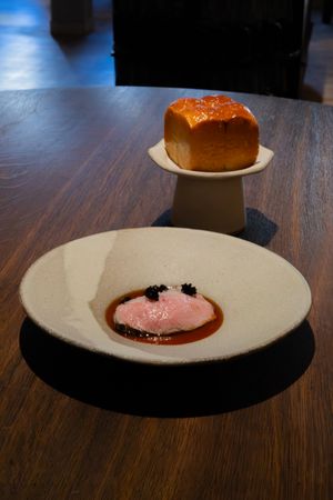 An elegant plate with pink mousse and garnish sits on a wooden table with artisanal bread in the background.