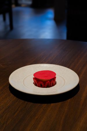 Bright red circular dessert presented on white plate against dark wooden surface.
