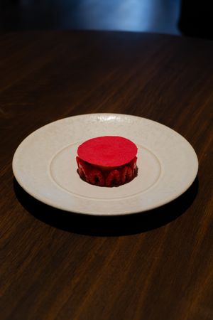 Vibrant red circular pastry centered on white ceramic plate on dark wood table.