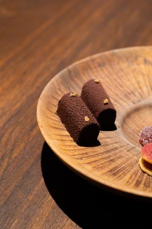 Close-up of a dark chocolate truffle resting on a wooden plate with dramatic lighting and shadows.